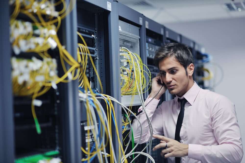 young business man computer science engeneer talking by cellphone at network datacenter server room asking  for help and fast solutions and services-1 (1)